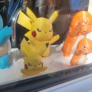 May include: A collection of plastic character figurines including two yellow Pikachu figures with pointed ears and red cheeks, two orange Charmander figures with cream-colored bellies, and a partial blue Squirtle figure, all displaying angry facial expressions.