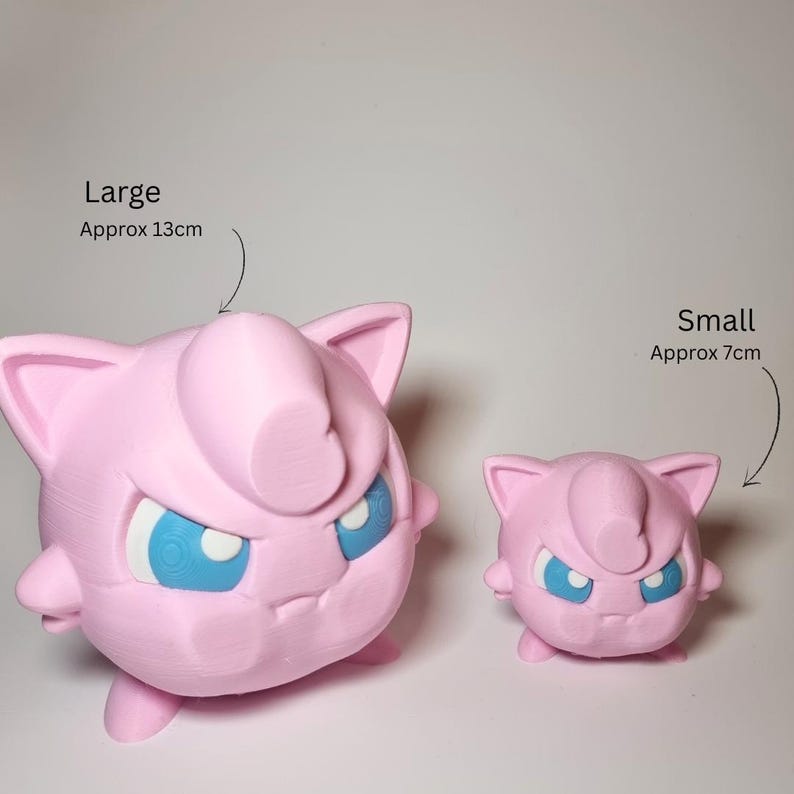 May include: Two pink spherical figures with pointed ears and blue eyes. The larger figure is labeled Large Approx 13cm and the smaller figure is labeled Small Approx 7cm. Both figures have a smooth, matte finish and a distinct curl on the forehead.