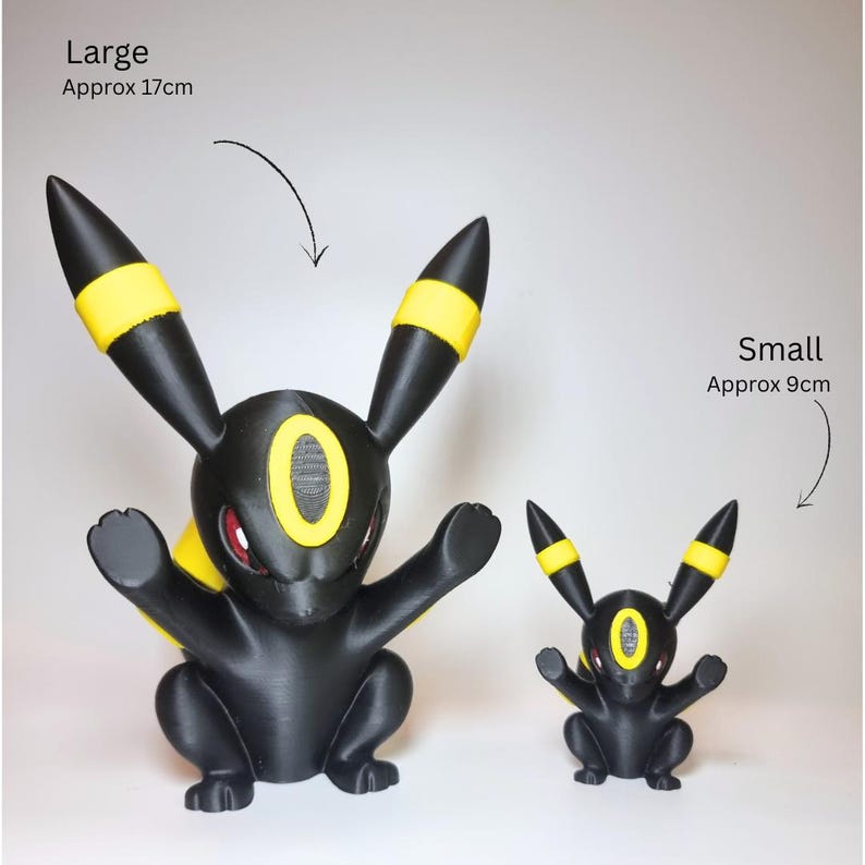 May include: Two black and yellow Umbreon figures with red eyes. The large figure is labeled Large Approx 17cm and the small figure is labeled Small Approx 9cm. Both figures have long ears with yellow bands and a yellow oval marking on the forehead.
