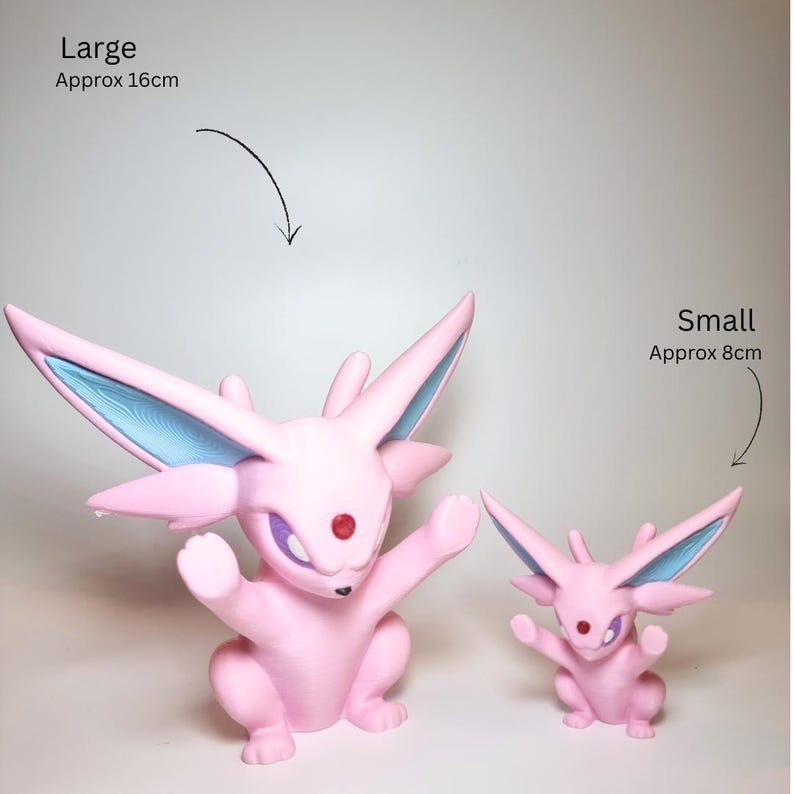 May include: Two pink creature figurines with large pointed ears, blue inner ear details, and a red gem on the forehead. The larger figure is labeled Large Approx 16cm, and the smaller figure is labeled Small Approx 8cm, indicating their relative sizes.