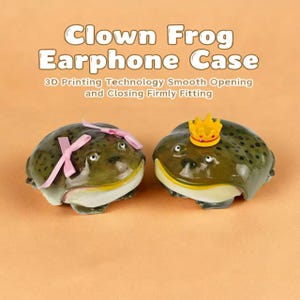 May include: Two novelty earphone cases shaped like frogs. One frog has a pink bow, the other a gold crown. The cases are olive green with black spots and white bellies. Text on the image reads "Clown Frog Earphone Case".