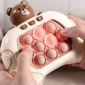 May include: A cream-coloured sensory toy with a bear-shaped top and bubble-popping buttons. The toy has pink accents and brown bear details. Buttons include power, volume, and mode selection. A fun, tactile toy.