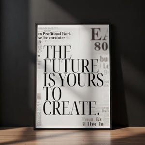 May include: A framed black and white print with the text "THE FUTURE IS YOURS TO CREATE" in bold, black letters. The background appears to be a newspaper print. The print is displayed on a wooden floor.
