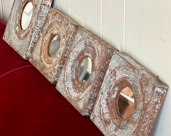 Puede incluir: Cinco pequeños espejos cuadrados de metal con un acabado de pintura blanca desgastada. Cada espejo tiene un inserto de vidrio redondo biselado. Los espejos están dispuestos en una fila, con el espejo más grande a la izquierda y el espejo más pequeño a la derecha.