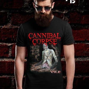 Puede incluir: Una camiseta negra de manga corta con un estampado gráfico de una figura pálida y cosida con brazos oscuros y texturizados. El texto CANNIBAL CORPSE aparece en rojo sobre la figura, y la palabra VILE está impresa en rojo en la parte inferior.