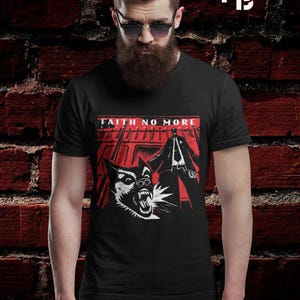 以下が含まれることがあります： 赤と白のグラフィックデザインが施された黒いTシャツ。デザインには、「FAITH NO MORE」の文字と、牙をむいた犬とコートを着た人物のイラストが含まれています。Tシャツは、あごひげとサングラスをかけた人が着用しています。