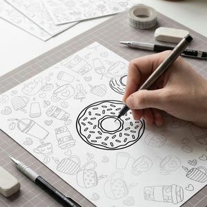 May include: A person's hand drawing a donut illustration with a pen on a white paper. The paper is covered with coffee and donut doodles. A cup of coffee, pencils, and tape are on the table.