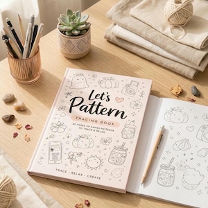 May include: A pink tracing book titled "Let's Pattern" with kawaii patterns, open to a blank page with a pencil. The book is on a wooden table with a succulent, pencils, and linen cloths.