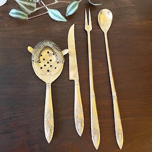 Puede incluir: Un juego de cuatro herramientas de bar doradas con mangos adornados. El juego incluye un colador de cócteles, un cuchillo de bar, un tenedor de cócteles y una cuchara de bar.