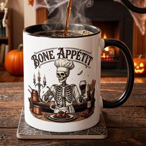 May include: A white ceramic mug with a black interior and handle, featuring a graphic of a skeleton chef wearing a hat and apron. The text "BONE APPÉTIT" is printed above the skeleton, who is holding a ladle and a wine glass near a table.