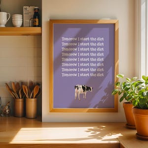 Puede incluir: Un cuadro enmarcado con fondo morado y el texto "Tomorrow I start the diet" repetido varias veces. Una ilustración de vaca en blanco y negro en la parte inferior. El marco es de color marrón claro.