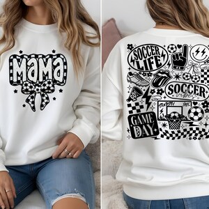 May include: White sweatshirt with "Mama" in a black and white soccer ball design on the front. The back features soccer-themed graphics, including "Soccer Life," a soccer ball, and a basketball hoop. The sweatshirt is a casual, sporty style.
