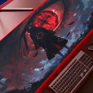 May include: A large rectangular mouse mat with an anime-style illustration. The design features a figure in a black cloak with red accents, set against a dark, fiery background with a large red eye. A keyboard and mouse are visible.