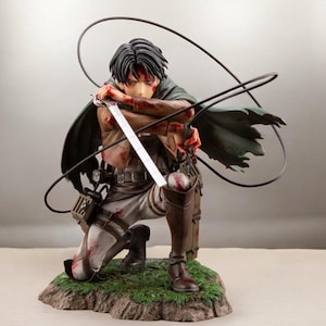 May include: A detailed figurine of a kneeling character from the anime series Attack on Titan. The figure is clad in a military uniform, holding a sword, and features blood-like details. The figure is posed on a small, grassy base with a wire apparatus.