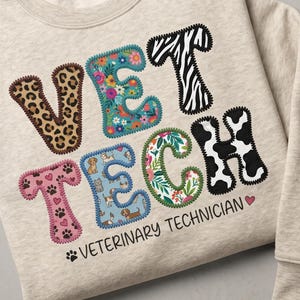 Puede incluir: Sudadera beige con las palabras "VET TECH" en letras coloridas y estampadas. Las letras están decoradas con estampados de animales, diseños florales e ilustraciones de perros. El texto "VETERINARY TECHNICIAN" está debajo.