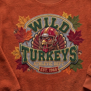 May include: A textured orange sweatshirt featuring a circular graphic with a turkey wearing a football helmet. The text reads WILD TURKEYS ATHLETIC DEPT. EST. 1968. The design is surrounded by embroidered-style autumn leaves and small acorns.