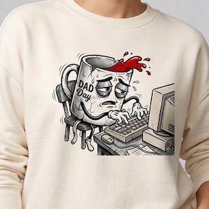 Op de afbeelding: Een crèmekleurige sweater met ronde hals en een grafische illustratie van een vermoeide, gebarsten koffiemok die aan een bureau zit en op een computer typt. De mok heeft een droevige uitdrukking, rode vloeistof die eruit morst en de tekst DAD Day.