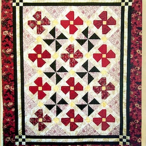 May include: A quilt pattern with a red, white, and black color scheme. The pattern features a repeating design of red flowers with yellow centers and black triangles. The quilt is 64 inches by 78 inches and is titled "Humble Bee Quilt Works".
