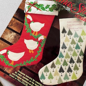 May include: Two Christmas stockings. One is red with white geese and green holly. The other is off-white with green, black, and tan trees. Text on the off-white stocking reads "MERRY CHRISTMAS from tiny seeds up wondrous trees grow."