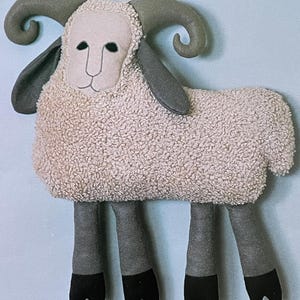 May include: A plush toy sheep with brown curly horns, a beige fluffy body, and gray and black legs.