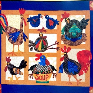 May include: A rectangular fabric quilt featuring a dark blue border with corner squares. The center displays six panels with various chickens and birds in colorful patterned fabrics. One central panel shows a chicken sitting in a bowl labeled SOUP.