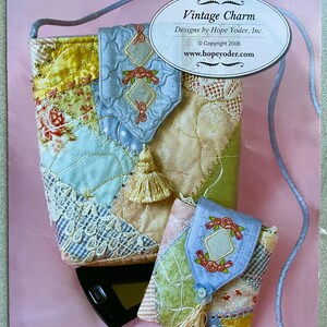 May include: A vintage charm quilted cell phone pouch with a blue and white floral design. The pouch has a tassel and a strap. The pouch is on a pink background. Vintage Charm Designs by Hope Yoder, Inc. Copyright 2006. www.hopeyoder.com