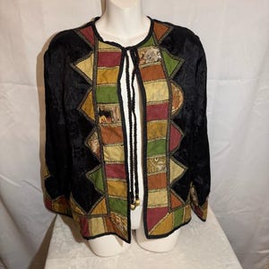 May include: Black open-front jacket with a patchwork design. The jacket features a mix of colors including red, green, gold, and brown. The sleeves and body are black with a textured pattern. A black tie closure is at the neckline.