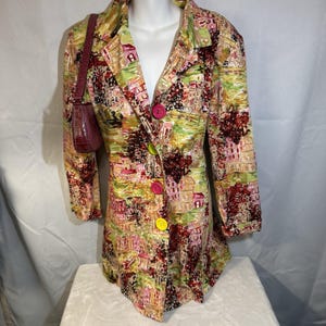 May include: A long-sleeved blazer with a colorful cityscape print, featuring pink, green, and yellow hues. The blazer has a button closure with pink and yellow buttons. A small, burgundy handbag hangs on the left side.
