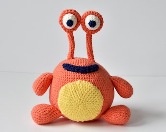May include: A crocheted orange and yellow monster toy with blue eyes and a black mouth.