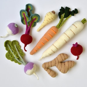 Op de afbeelding: Een verzameling gehaakte groenten, waaronder een wortel, pastinaak, raap, radijs en gember. De groenten zijn allemaal in verschillende kleuren en maten, en ze zijn in een willekeurig patroon op een witte achtergrond gerangschikt.