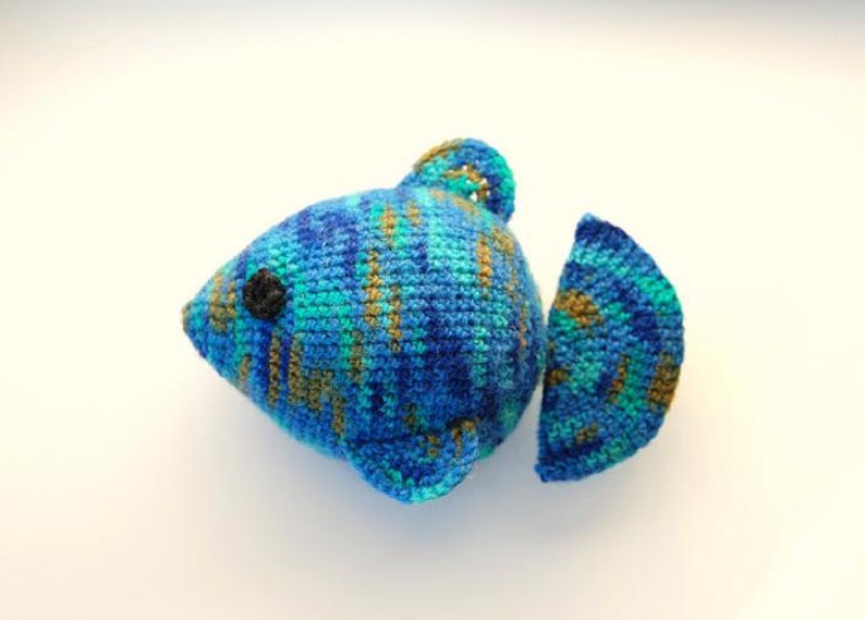 May include: A crocheted blue, green, and brown fish toy with a black eye.
