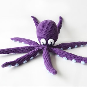May include: A handmade purple crochet octopus with white and blue accents. The octopus has eight long tentacles and large white eyes. The toy is made of soft yarn and is suitable for children.