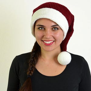 May include: A burgundy and white Santa hat with a white pom-pom. The hat is made of a knitted material. The hat has a white band around the bottom.