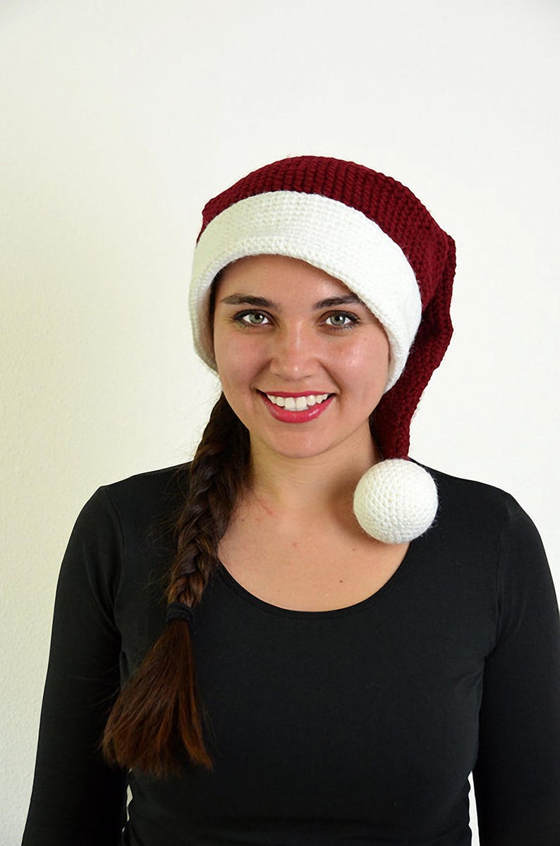 May include: A burgundy and white Santa hat with a white pom-pom. The hat is made of a knitted material. The hat has a white band around the bottom.