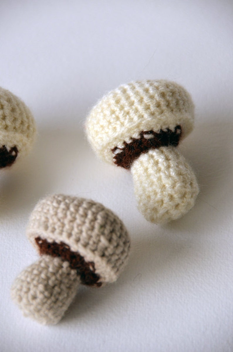 Op de afbeelding: Drie gehaakte paddenstoelen in beige en bruin. De paddenstoelen zijn gemaakt van zacht garen en hebben een textuur.