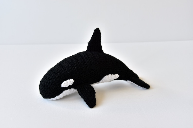 May include: A black and white crocheted orca whale plush toy. The orca has a white patch around its eye and a white underside.