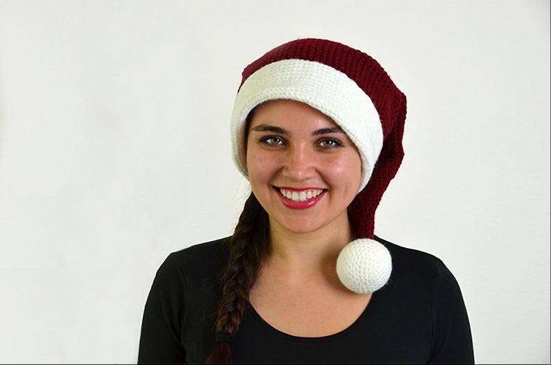 May include: A knitted Santa hat with a burgundy crown and a white brim and pom-pom. The hat is made of a soft, textured yarn. The hat is a festive accessory for the holiday season.