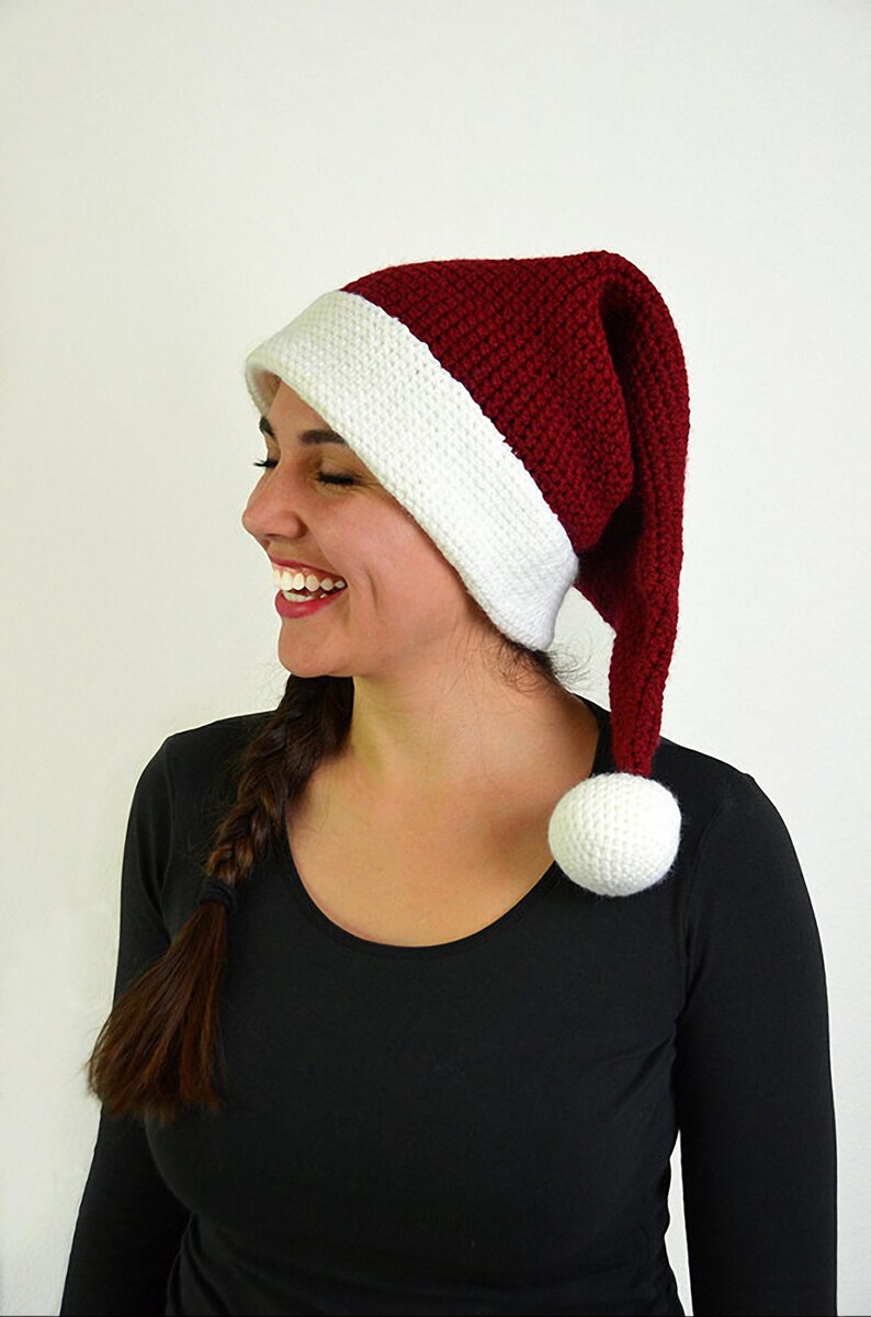 May include: A knitted Santa hat with a white brim and a red crown. The hat has a long, pointed end and a white pom-pom. The hat is worn by a person wearing a black long-sleeved shirt.