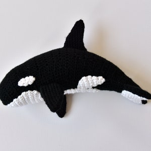 May include: A black and white crocheted orca whale plush toy. The orca has a white patch around its eye and white patches on its underside.