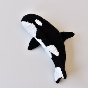 May include: A black and white crocheted orca whale plush toy. The orca has a white patch around its eye and a white patch on its belly.