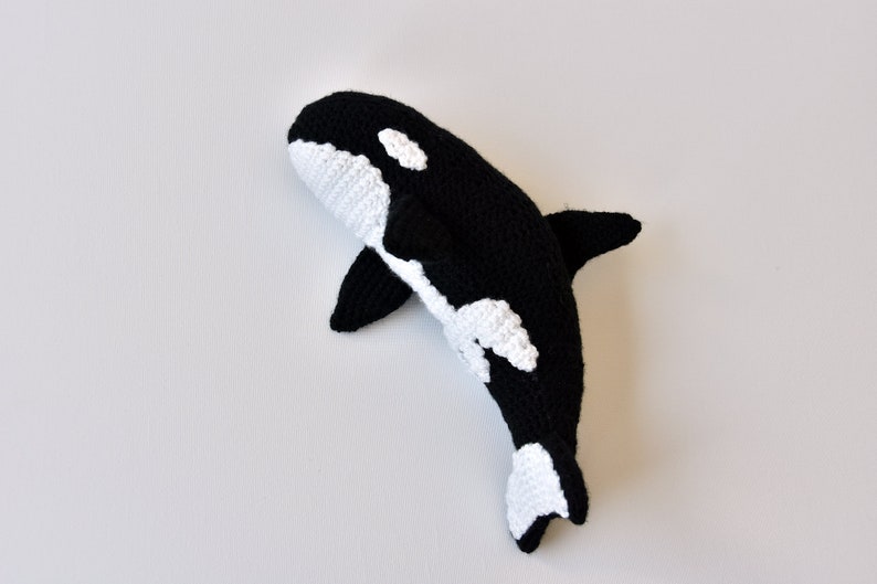May include: A black and white crocheted orca whale plush toy. The orca has a white patch around its eye and a white patch on its belly.