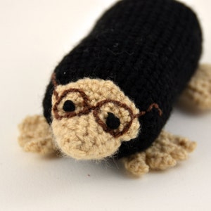 May include: A crocheted mole wearing glasses. The mole is black and brown and has a small, round nose.