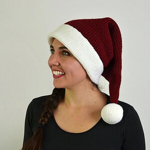 May include: A burgundy and white Santa hat with a long, pointed shape and a white pom-pom. The hat is made of a textured knit material and has a white band at the base. A festive accessory for the holiday season.