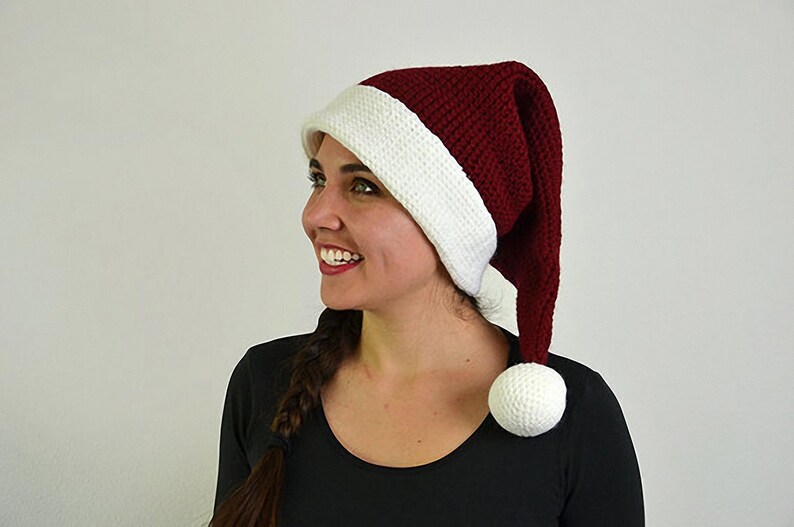 May include: A burgundy and white Santa hat with a long, pointed shape and a white pom-pom. The hat is made of a textured knit material and has a white band at the base. A festive accessory for the holiday season.