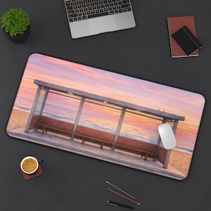 Könnte beinhalten: Rechteckige Schreibtischunterlage mit einer Strand-Szene bei Sonnenuntergang, die eine Bushaltestelle zeigt. Die Matte hat ein farbenfrohes Design, mit einer Computermaus und einer Kaffeetasse auf einer dunklen Oberfläche.