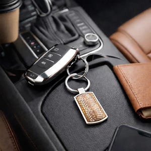 May include: A rectangular keychain featuring a textured, tan and brown snakeskin-patterned inlay set within a polished silver-tone metal frame, attached to a circular split ring connected to a black and silver automotive key fob.