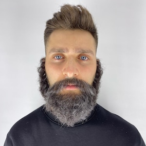 May include: A man with blue eyes, brown hair, and a full, graying beard. He is wearing a black crew neck sweatshirt. The background is a plain white.