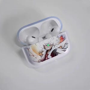 Op de afbeelding: Transparante beschermhoes voor draadloze oordopjes, met een kleurrijke illustratie in anime-stijl. Het ontwerp toont een personage met groene ogen en een brede grijns, tegen een witte en oranje achtergrond. De hoes is open en toont de witte oordopjes.