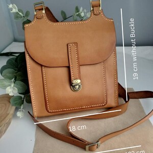 May include: A tan leather crossbody bag with an adjustable strap. The bag has a flap closure with a metal clasp and a small front pocket. The bag is 19 cm without the buckle and 18 cm wide. The adjustable strap is 42.9 to 48 inches.