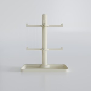 May include: A cream-colored mug tree with a rectangular base, a central pole, and two tiers of hooks for hanging mugs. The top of the pole has a small handle. The design is minimalist and modern.